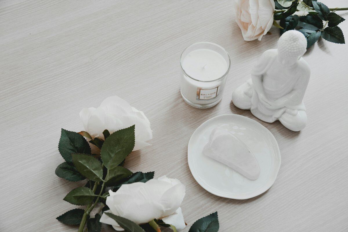 Candle, gua sha stone and white roses on a table